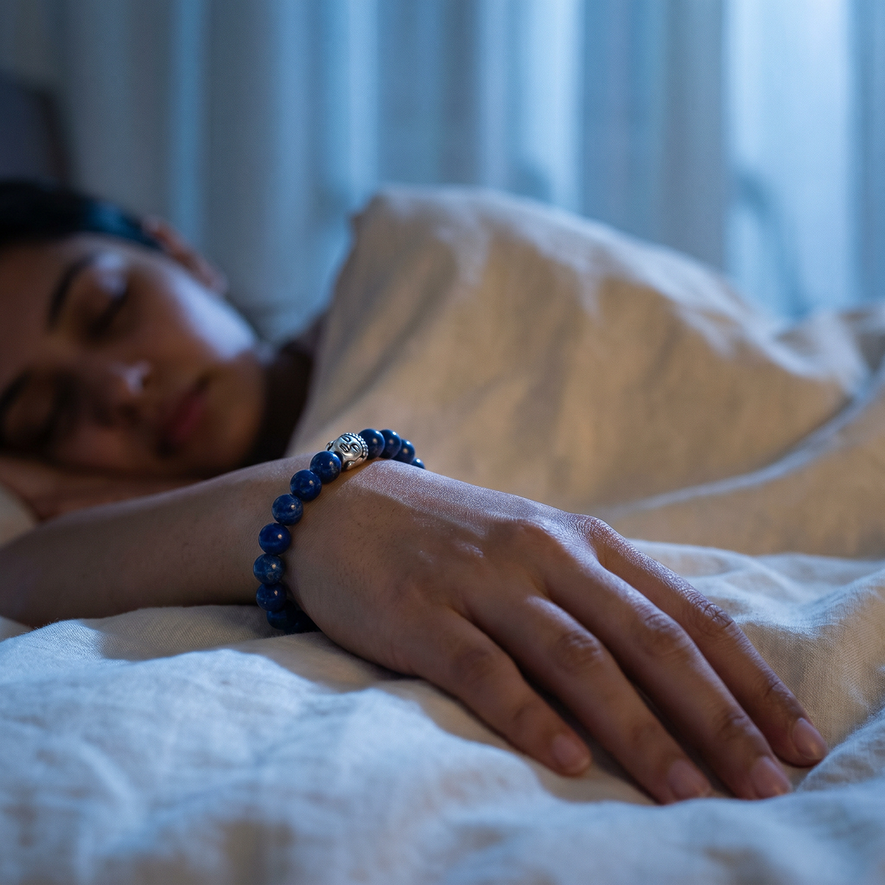 Person sleeping in bed with a blue beaded bracelet on wrist